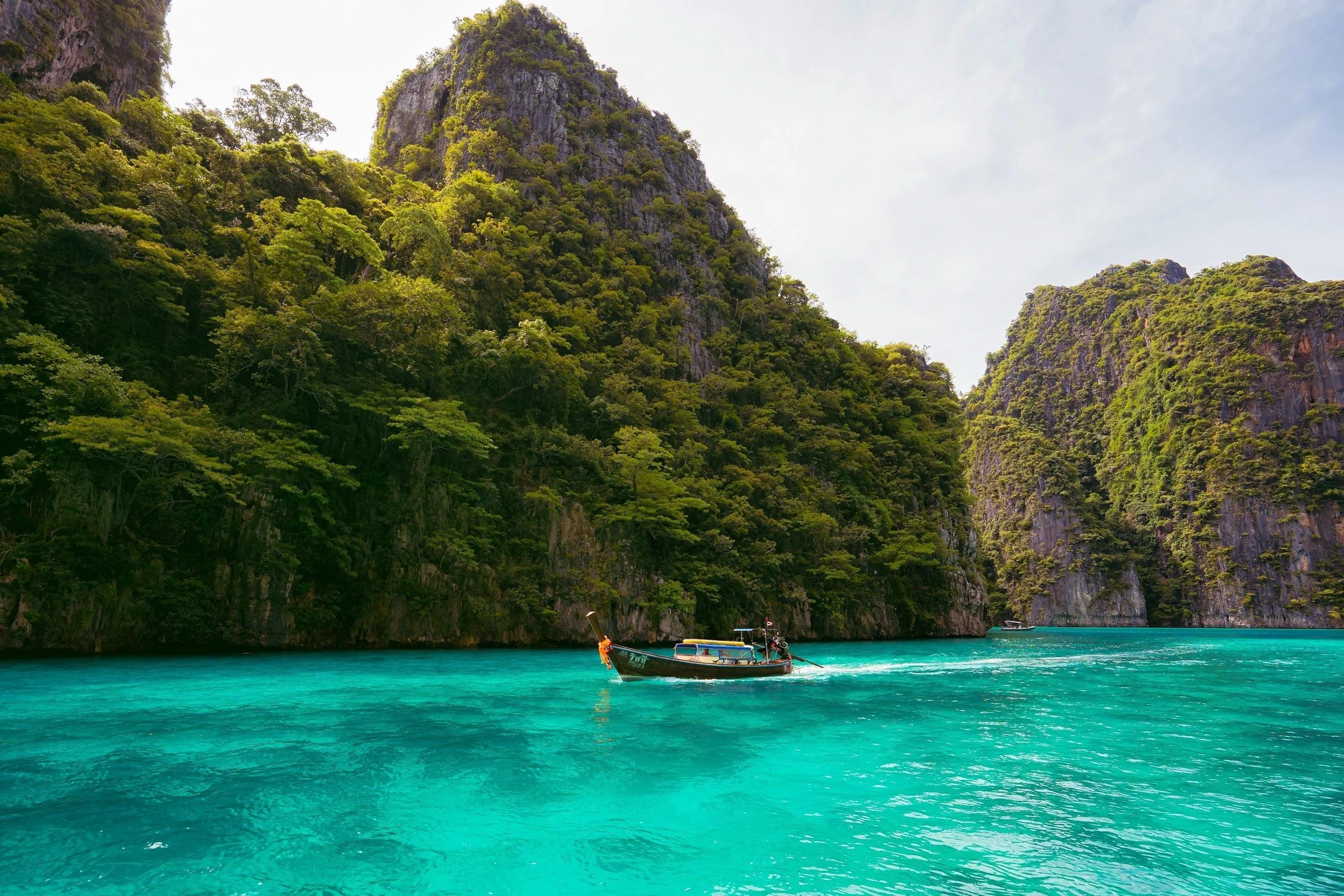 A long-tail boat on turquoise water between tall limestone cliffs in the Phi Phi Islands.