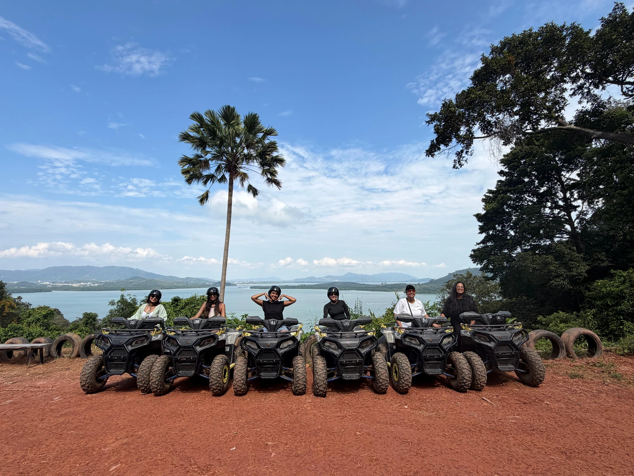 Fila de quads y participantes en una explanada con una palmera y vistas al mar.