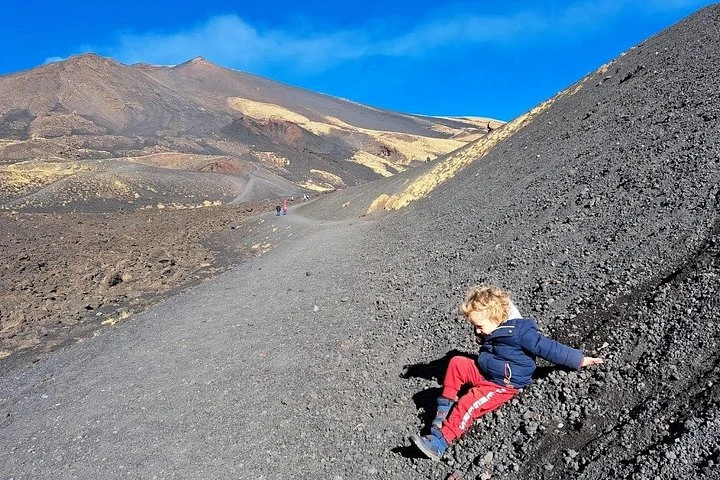 Enfant assis sur une pente de cendres de l’Etna près d’un sentier