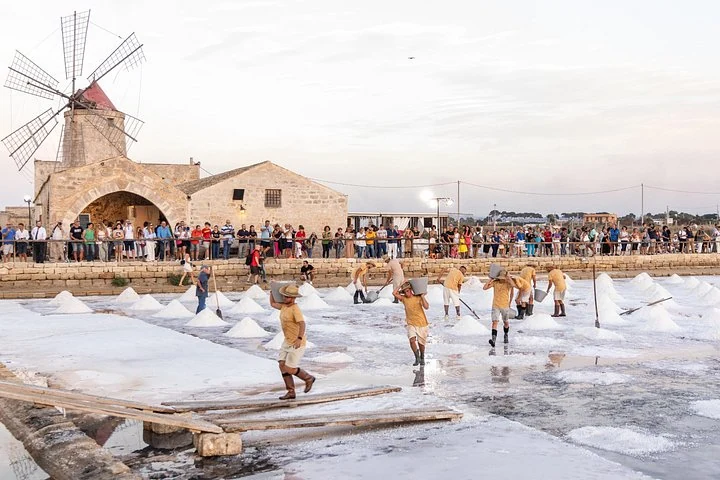 Personnes avec des pelles entre les tas de sel devant le moulin des salines Culcasi à Nubia