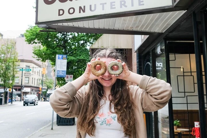 Une visiteuse tient deux donuts devant l’enseigne d’une boutique de Vancouver.