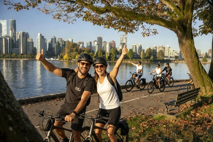 Deux cyclistes posent près de la promenade du front de mer, avec les immeubles de Vancouver de l’autre côté de l’eau.