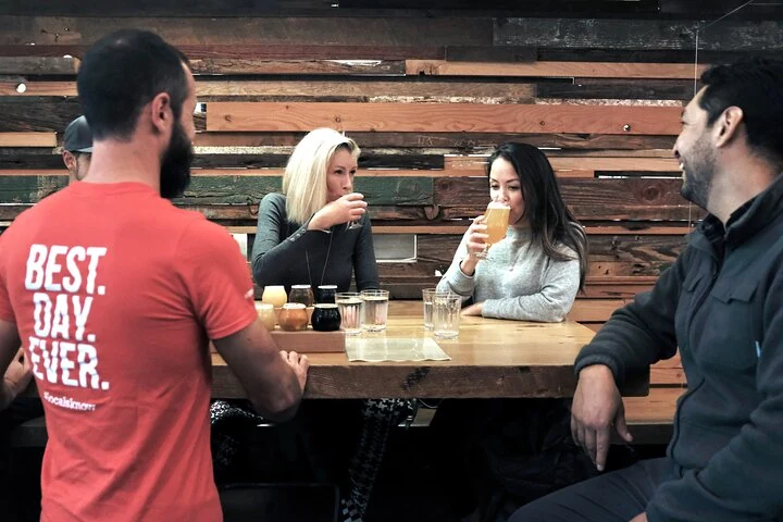 Eine kleine Gruppe probiert Bier an einem Holztisch während einer Brauereitour in Vancouver.