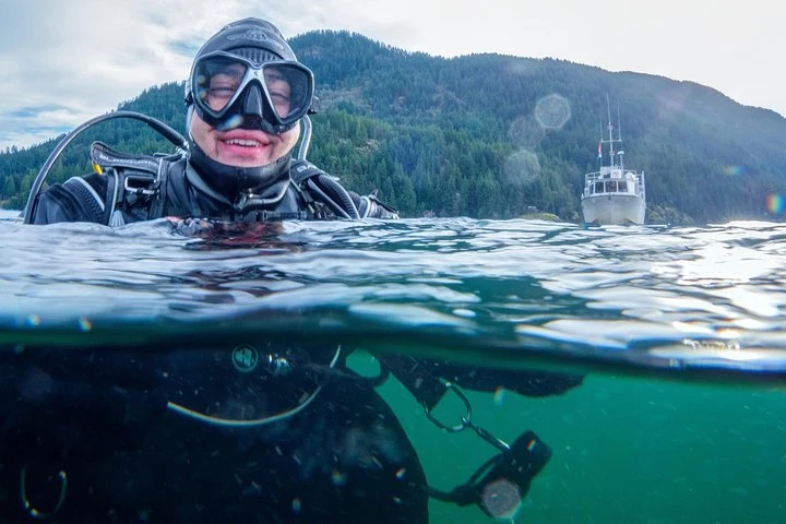 Eine Person mit Maske und Tauchausrüstung an der Wasseroberfläche des Howe Sound, mit einem Boot dahinter, außerhalb von Vancouver.