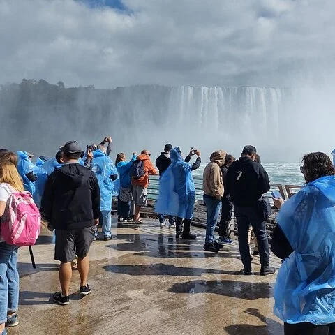 Des visiteurs en ponchos bleus photographient les chutes depuis une plateforme mouillée.