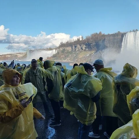 Un groupe en ponchos jaunes se rassemble sur une surface mouillée, avec des cascades et de la brume à l’arrière-plan.