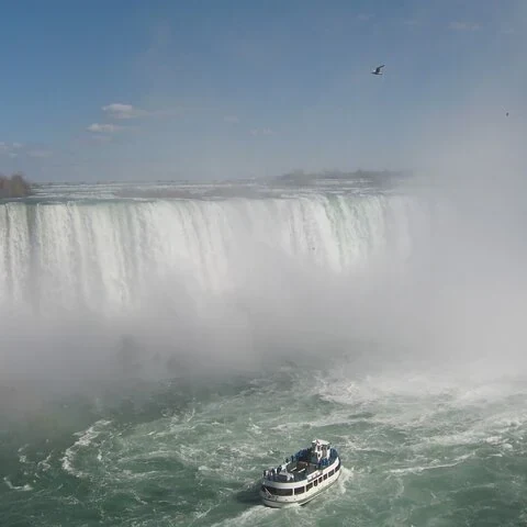Un petit bateau devant une large chute d'eau et un nuage de brume.