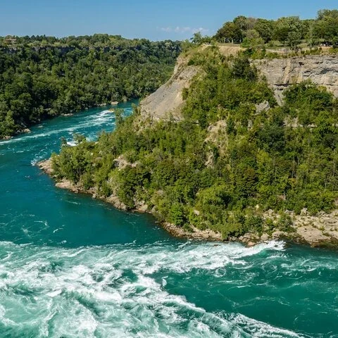 A river of turquoise water and white foam runs through a gorge with rocky slopes covered in greenery.