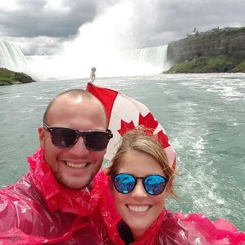 Two visitors wearing red ponchos and sunglasses pose in front of the falls.