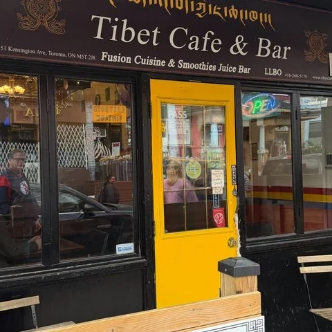 A storefront displaying the Tibet Cafe & Bar sign, with a yellow door and windows on either side.
