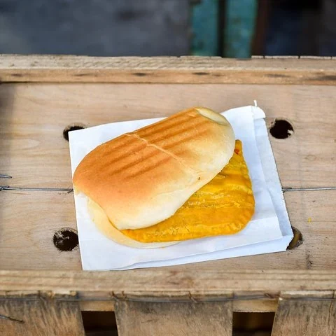 A sandwich with a yellow filling on paper and a wooden tray.