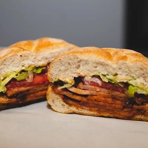 Ein halbiertes Sandwich mit Fleisch, grünen Blättern und Tomate.