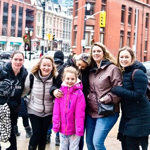 Eine Gruppe, darunter ein Kind mit rosa Jacke, posiert auf einer Straße neben Backsteingebäuden.