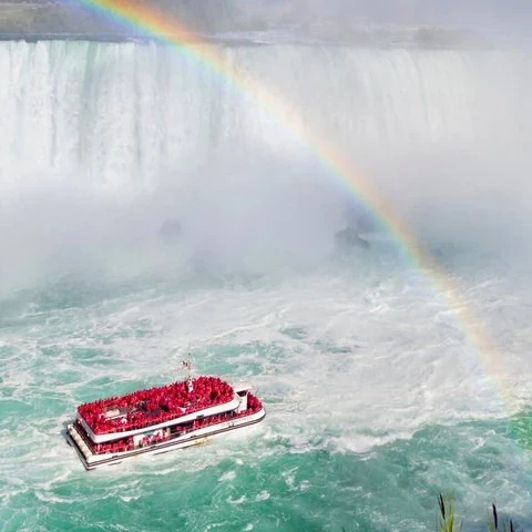 Un barco con pasajeros de ponchos rojos bajo un arcoíris frente a las cataratas.