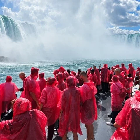 Personas con ponchos rojos ocupan una cubierta abierta, con grandes caídas de agua y bruma al fondo.