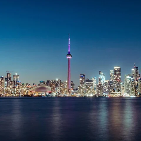 Die beleuchtete Skyline von Toronto spiegelt sich nachts im Wasser.