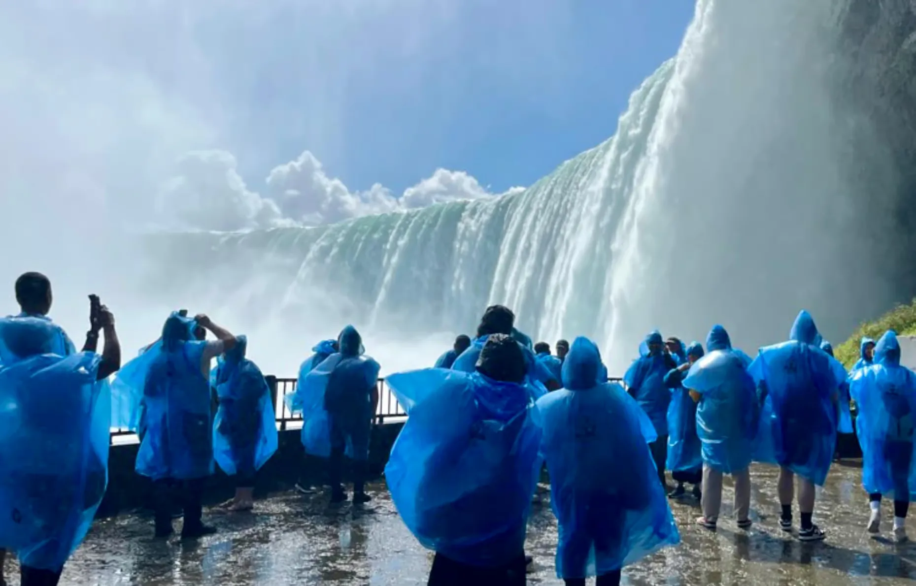 Visitors in blue ponchos watch a large waterfall from a railing.