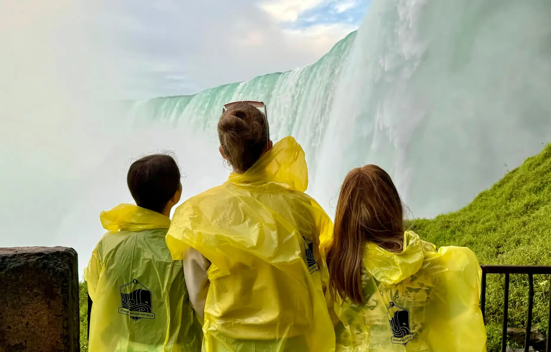 Three visitors in yellow ponchos watch the falls from a viewing area.
